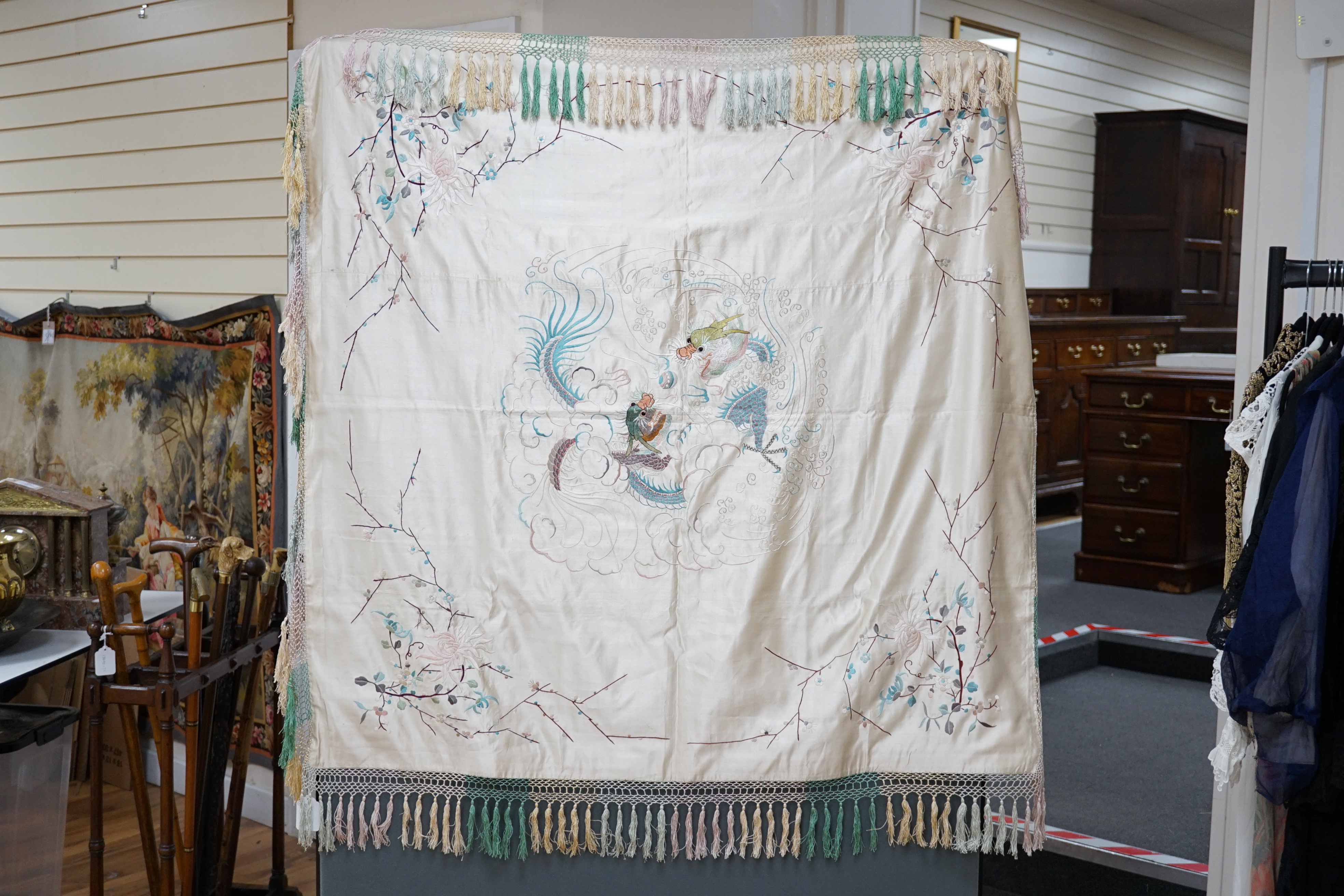 A 1920’s-30’s Chinese oyster silk satin embroidered shawl, now converted to a wall hanging, embroidered in pastel coloured silk threads, the large central motif of two dragons playing with a pearl, the corners of the han